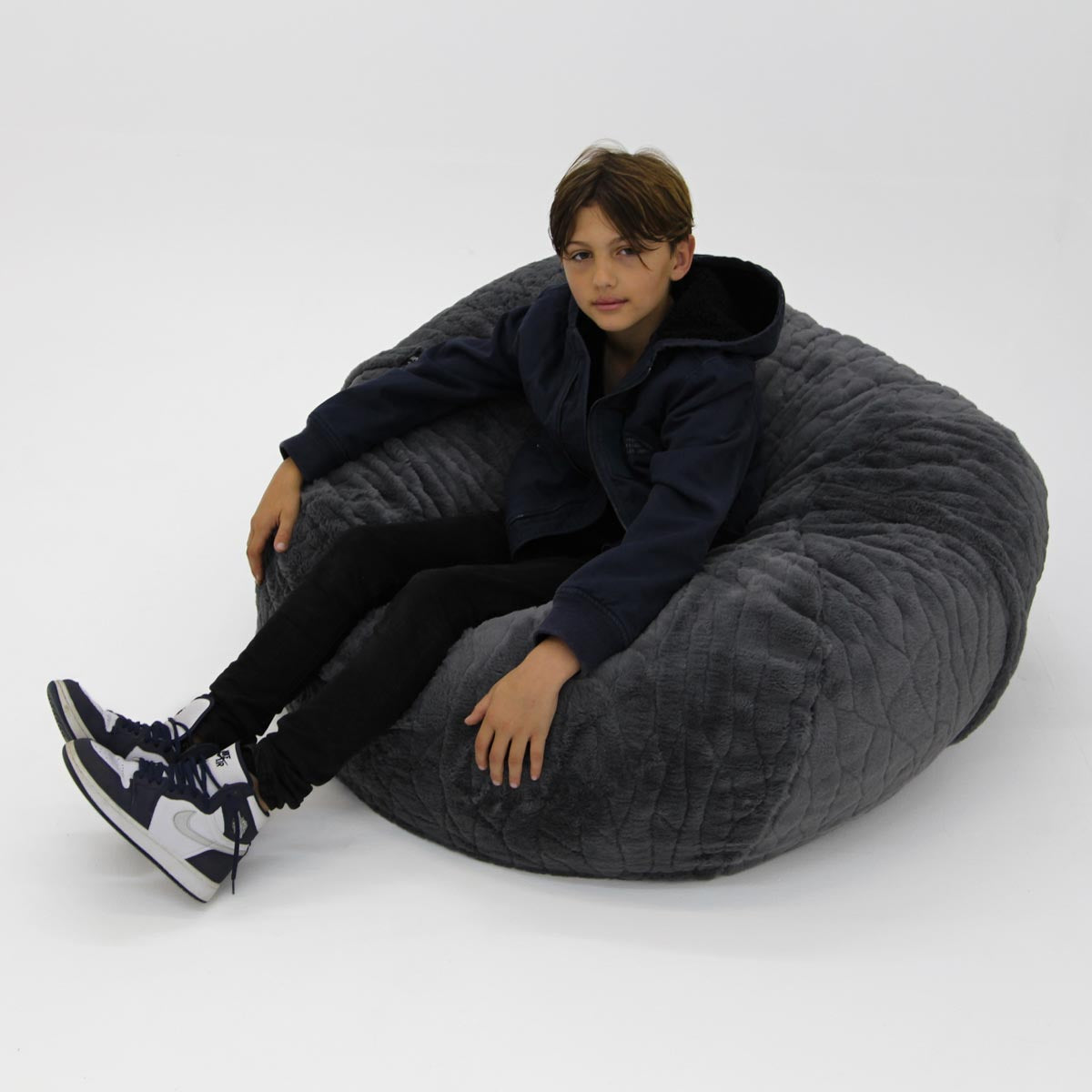 Child sitting on a large gray bean bag chair against a white background